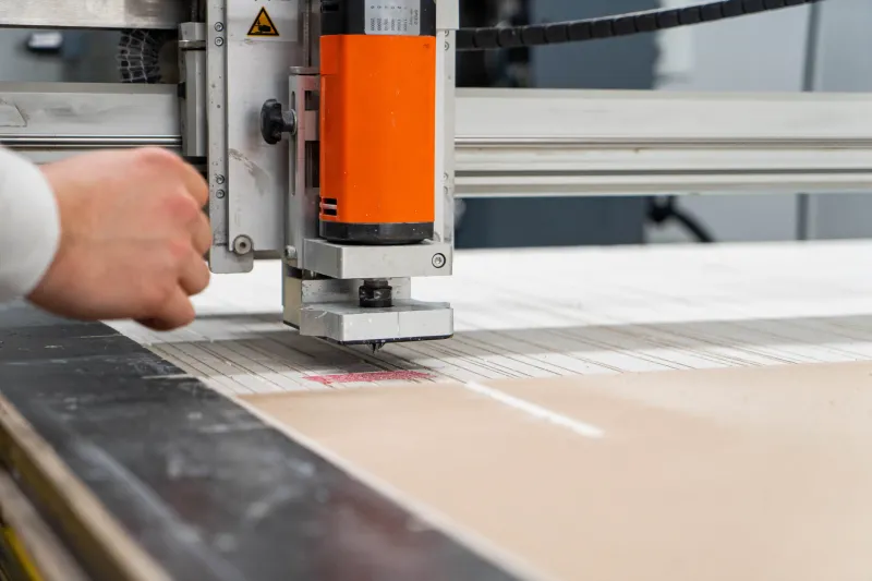 CNC-Fräse schneidet eine Platte zu, im Vordergrund die Hand des Bedieners am Maschinenportal.